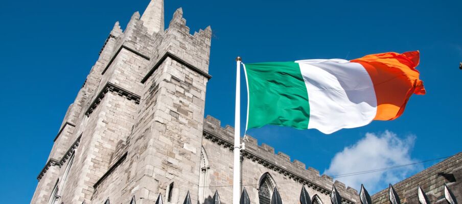 The flag of Ireland with a blue sky and a building in the background.
