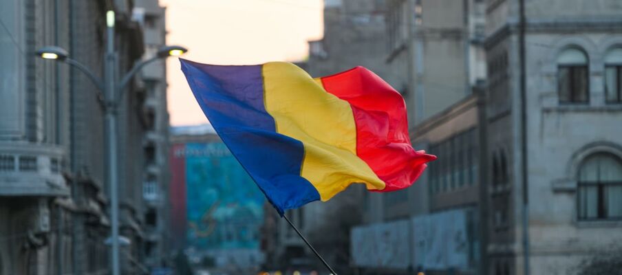 The flag of Romania with a city in the background showing busy streets.