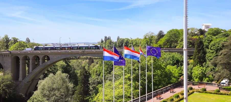 The flag of Luxembourg with a bridge and the national border in the background.