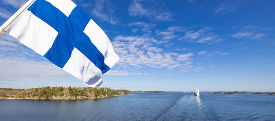 Flag of Finland with coast The flag of FInland with the sea and coastline in the background.