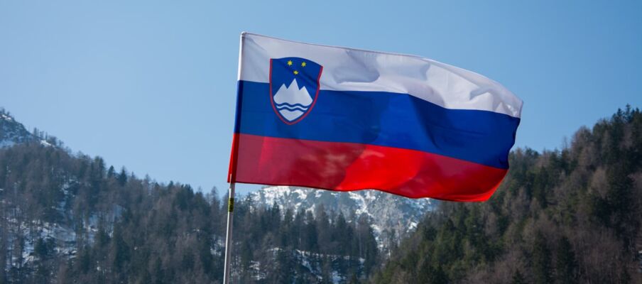 The flag of Slovenia with a blue sky and mountains in the background.